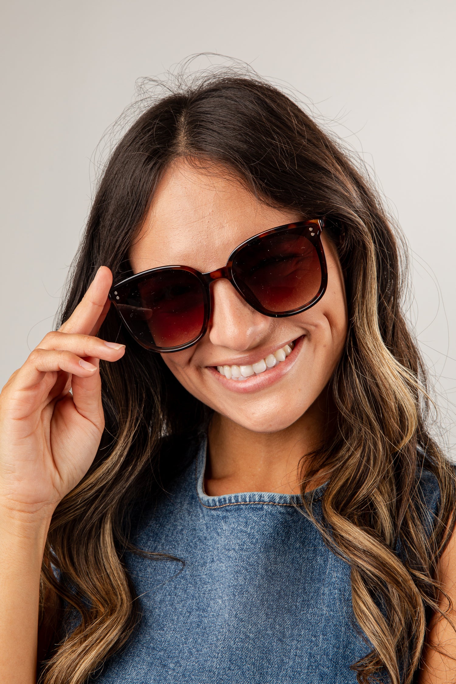 Woman wearing sunglasses and a denim top against a plain background