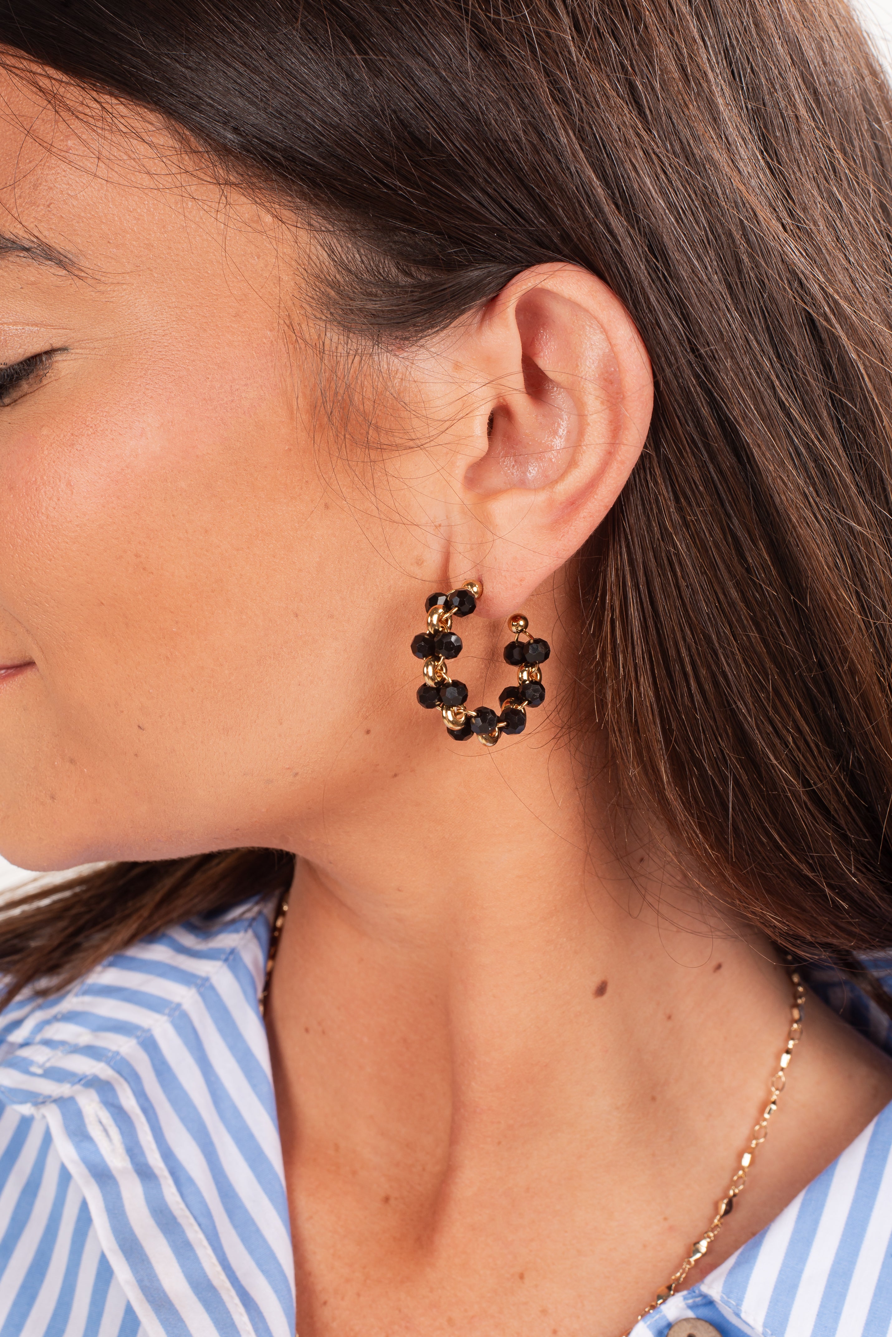 Close-up of a woman wearing gold hoop earrings with black beads.