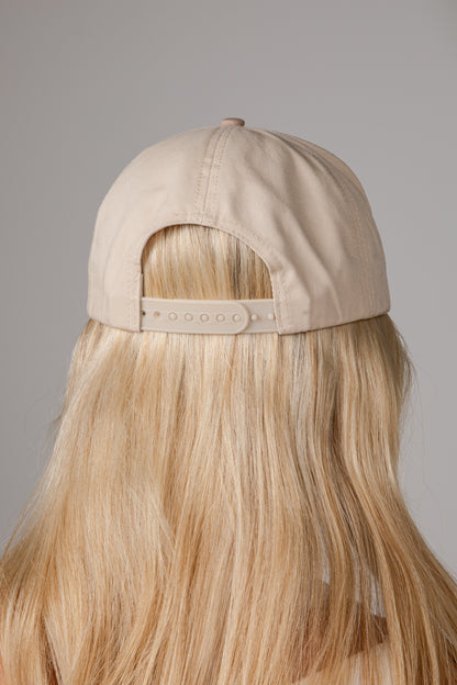 Back view of a beige baseball cap worn by a model with long blonde hair, shown against a neutral gray background.
