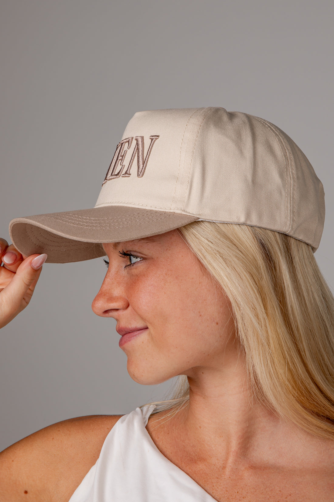 A woman in profile wearing a beige baseball cap with &