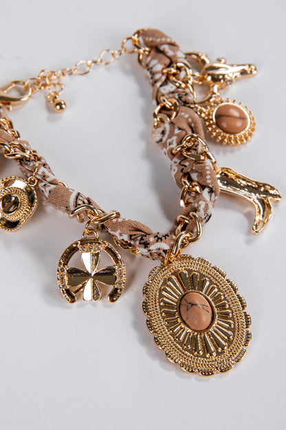 Gold charm bracelet with various charms on a light gray background