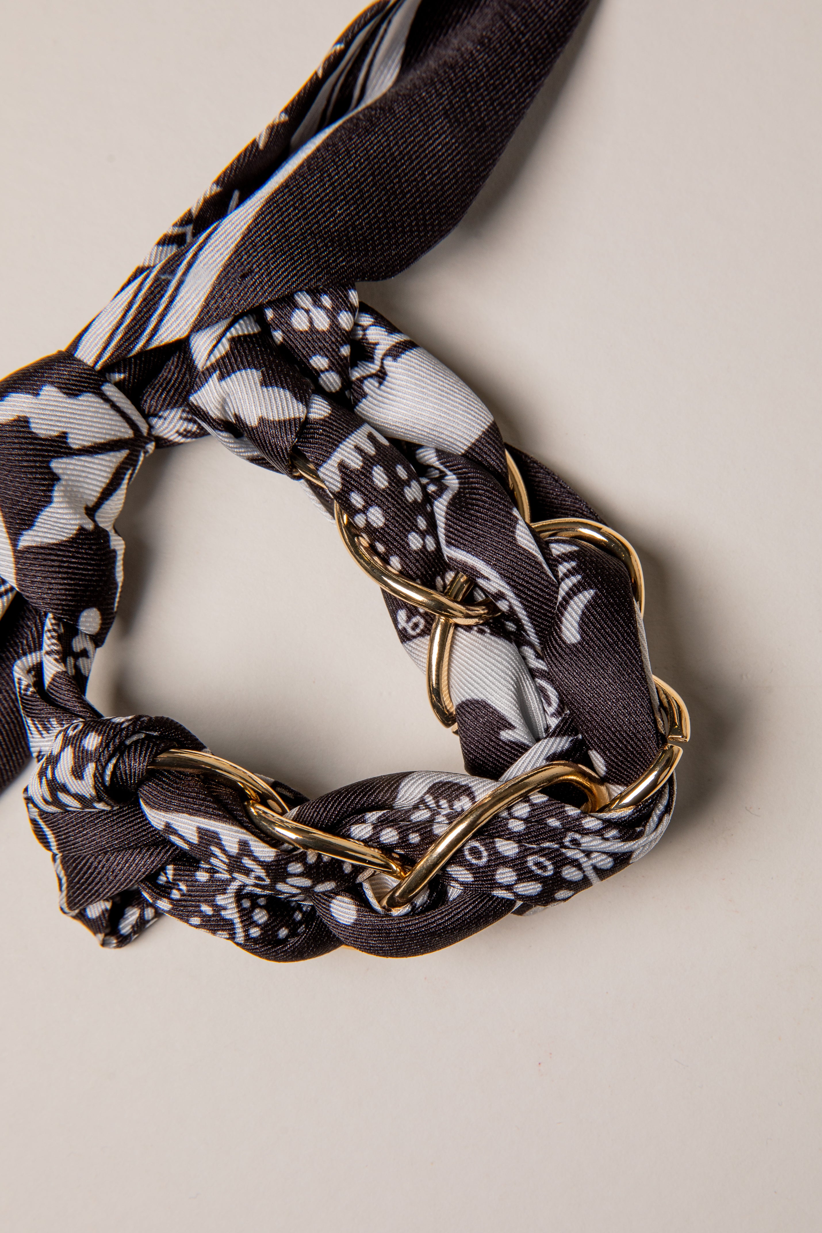 Scarf with gold chain detail on a neutral background