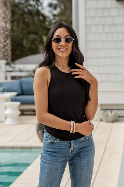 Woman wearing a black sleeveless top and blue jeans standing by a pool.