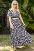 Woman in a black and white floral dress standing outdoors with greenery in the background