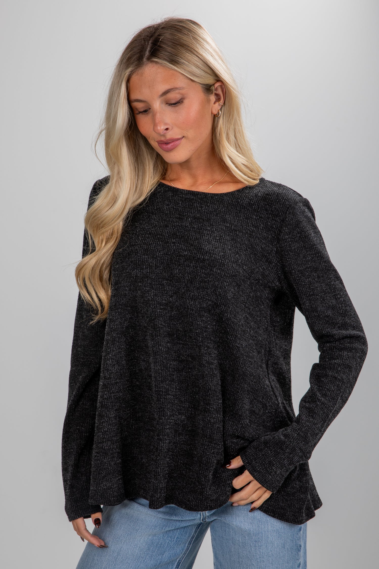 Woman wearing a black sweater and blue jeans on a gray background