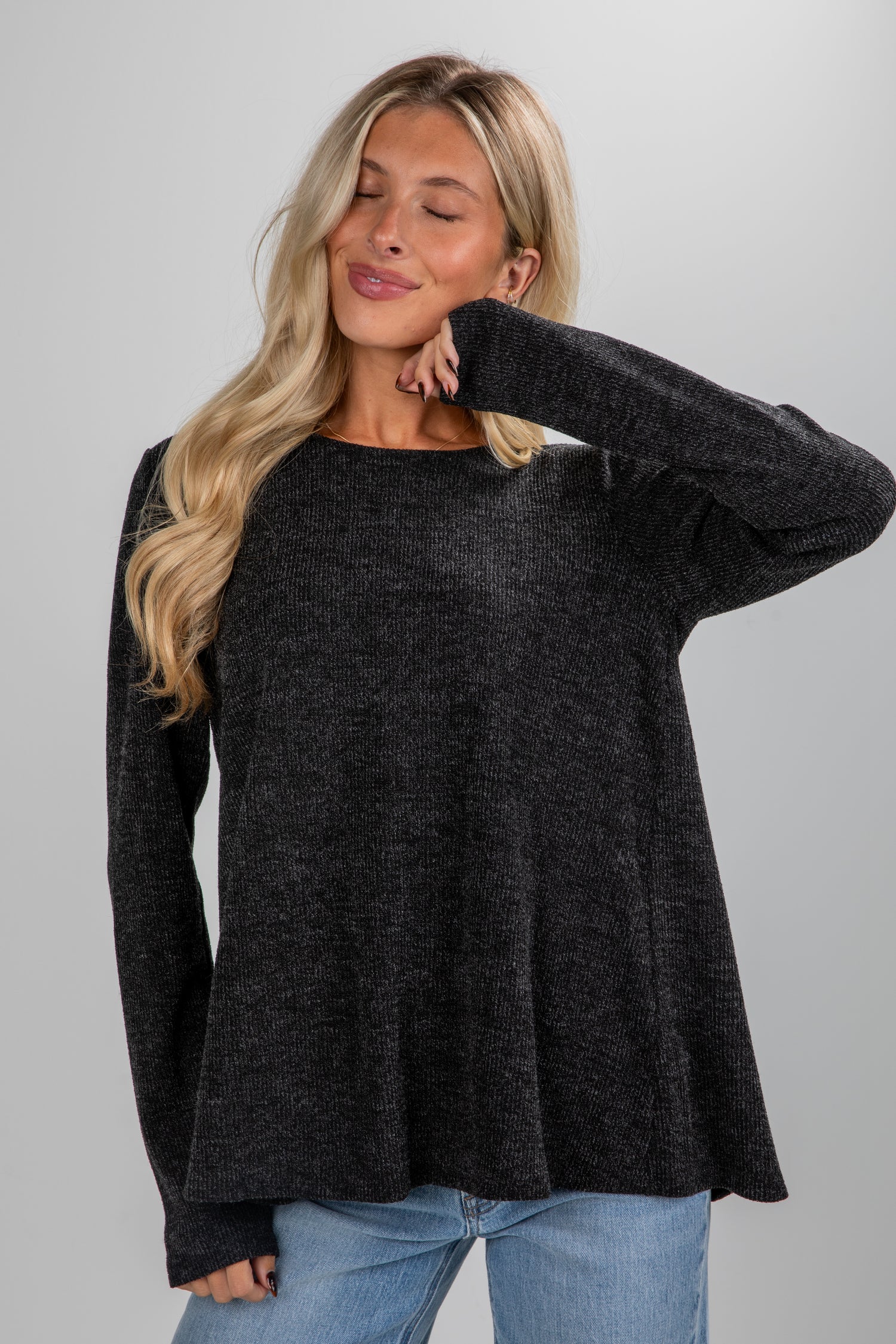 Woman wearing a dark gray sweater and blue jeans against a plain background