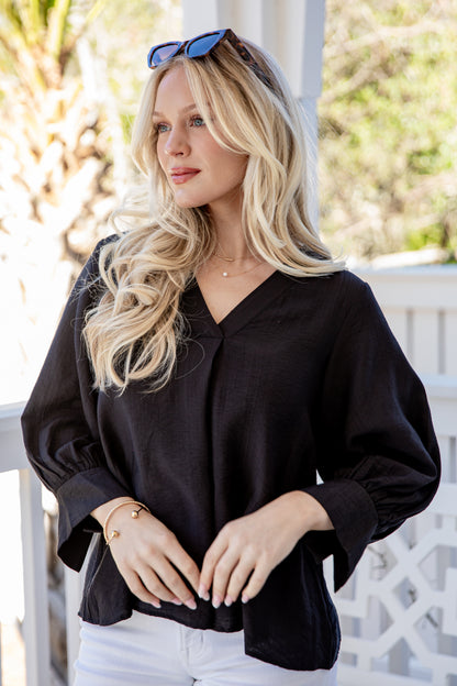 Woman wearing a black blouse with a blurred outdoor background