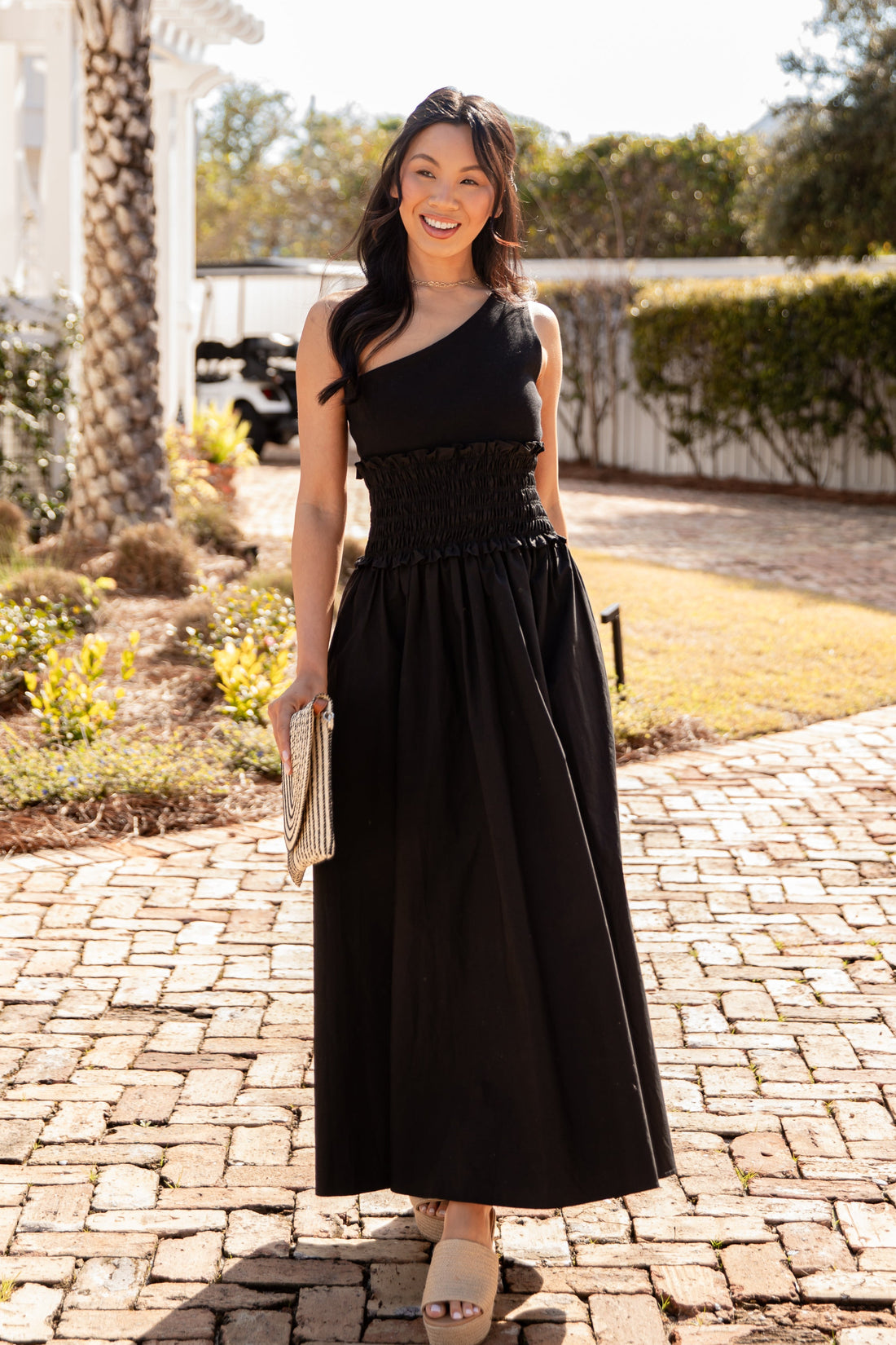 Woman in a black dress standing on a brick path with greenery in the background