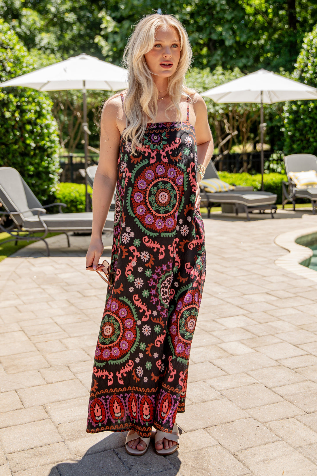 Woman in a colorful patterned dress standing in a garden with lounge chairs and umbrellas.