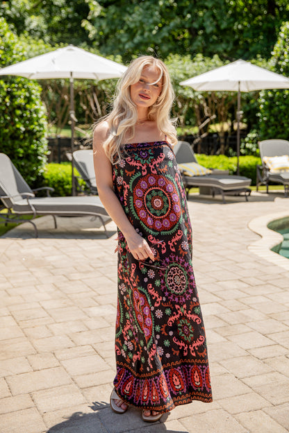 Woman wearing a colorful patterned dress standing outdoors near lounge chairs and umbrellas.