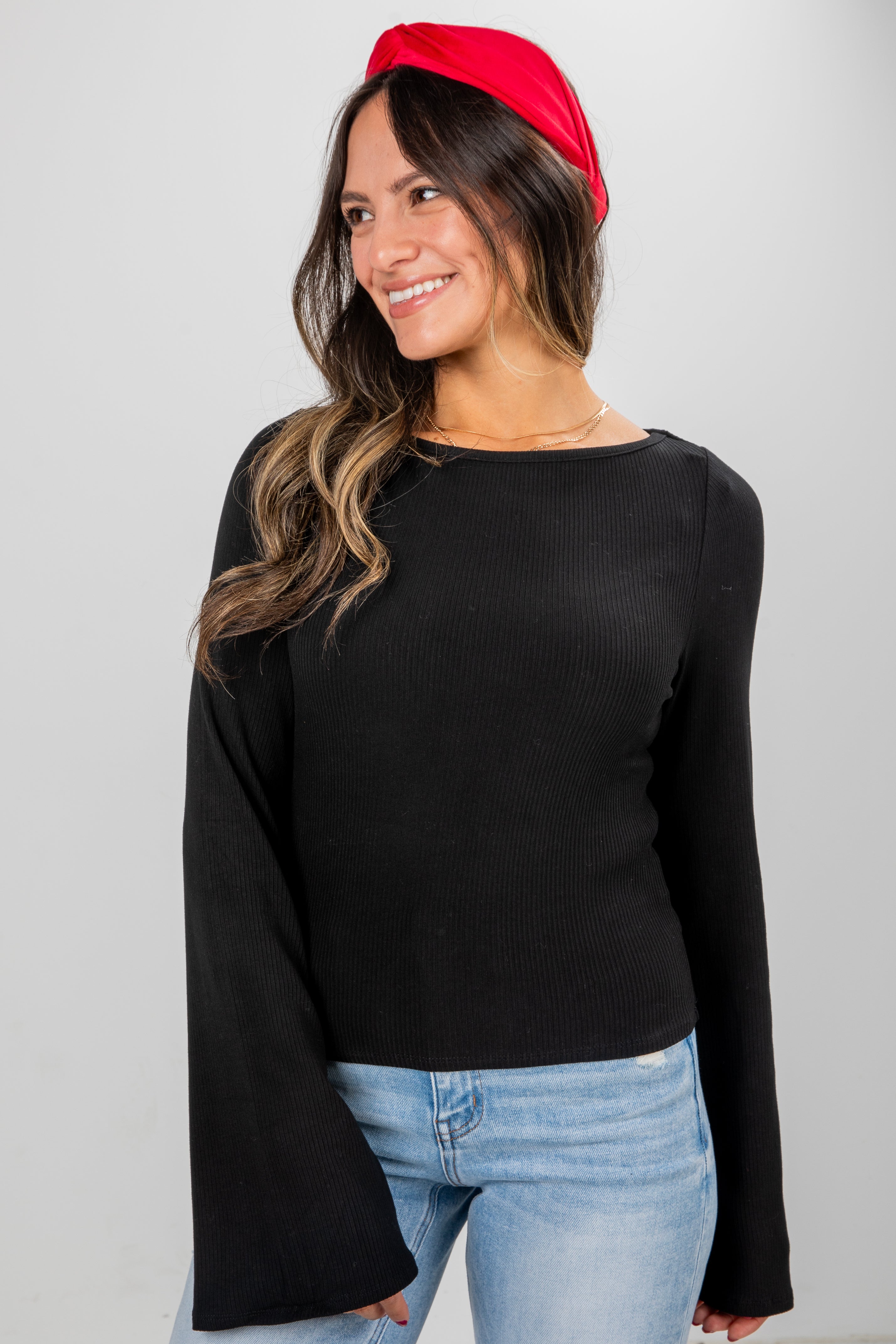 Woman wearing a black long-sleeve top and red headband on a gray background