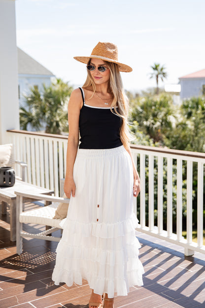 Woman in black tank top and white skirt on a balcony with palm trees in the background