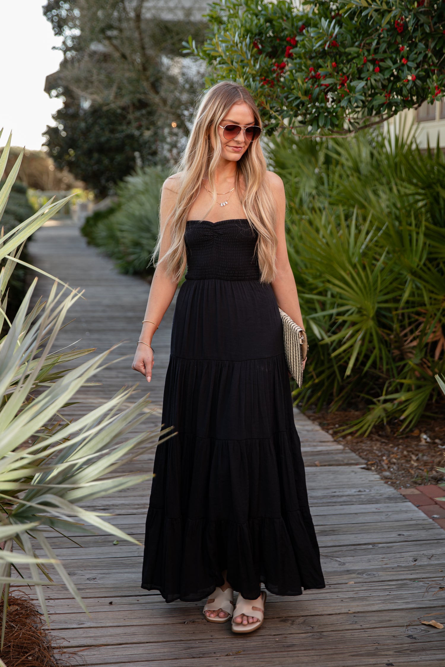 Woman in a black dress standing on a wooden path with greenery around.