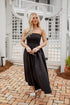 Woman in a black strapless dress standing on a brick patio.