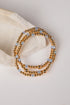 A stack of three beaded stretch bracelets with metallic gold beads and light blue faceted beads, displayed on a neutral cream-colored stone prop against a light background.