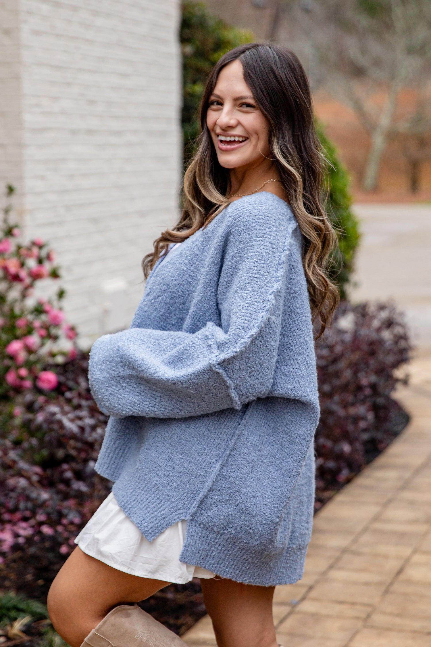 Woman wearing a blue sweater over a white dress standing outdoors.