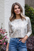 Woman wearing a floral blouse and blue jeans standing outdoors with plants in the background