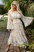 Woman in a floral dress standing on a patio with greenery in the background