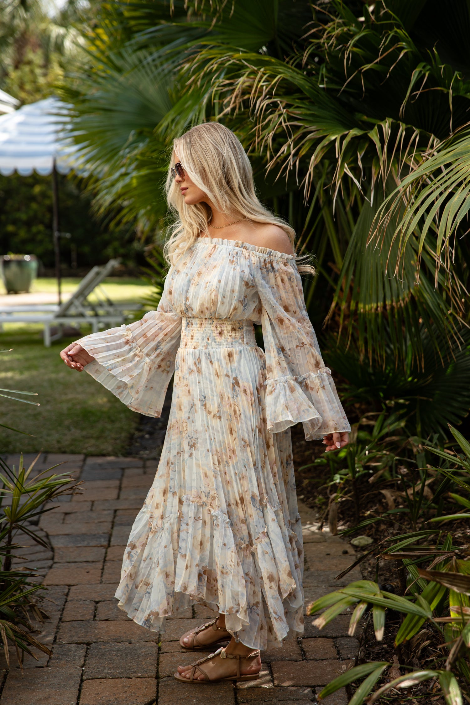 Woman in a floral off-shoulder dress standing outdoors with greenery around