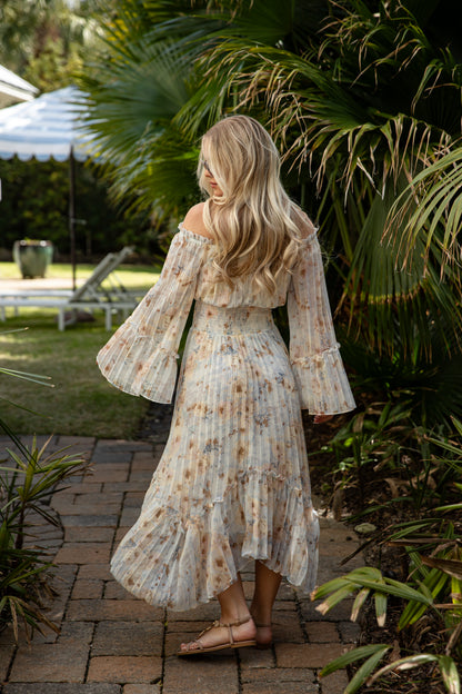 Woman in a floral dress standing on a brick path with greenery around