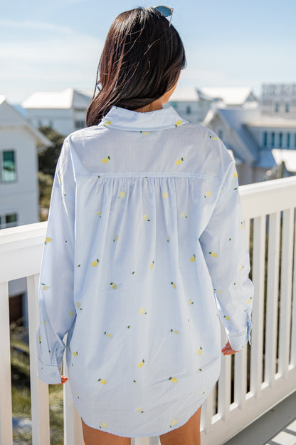 Woman wearing a light blue floral shirt on a balcony with a cityscape background