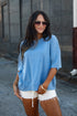 A woman wearing an oversized light blue t-shirt and white denim cutoff shorts, standing outdoors against a gray stone wall.