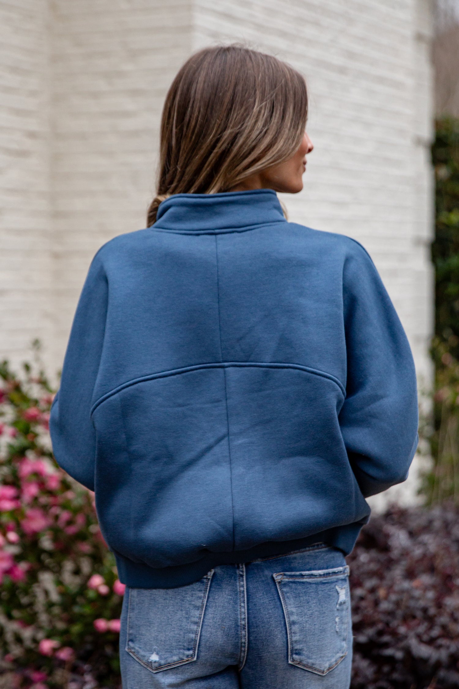 Person wearing a blue jacket standing in front of a building with plants in the background