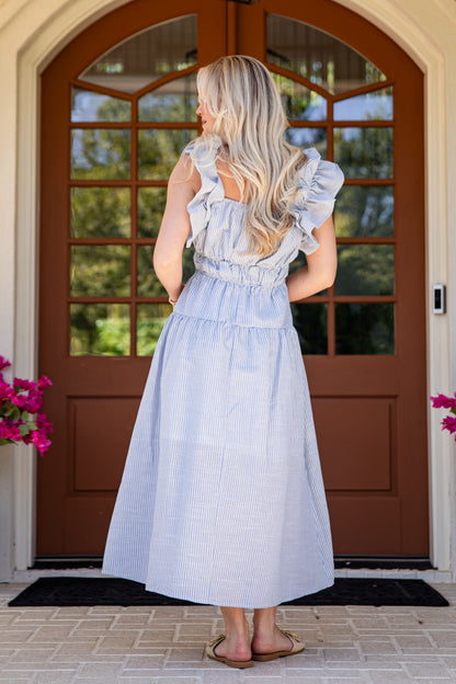 Woman in a light blue dress standing in front of a brown door with glass panels.