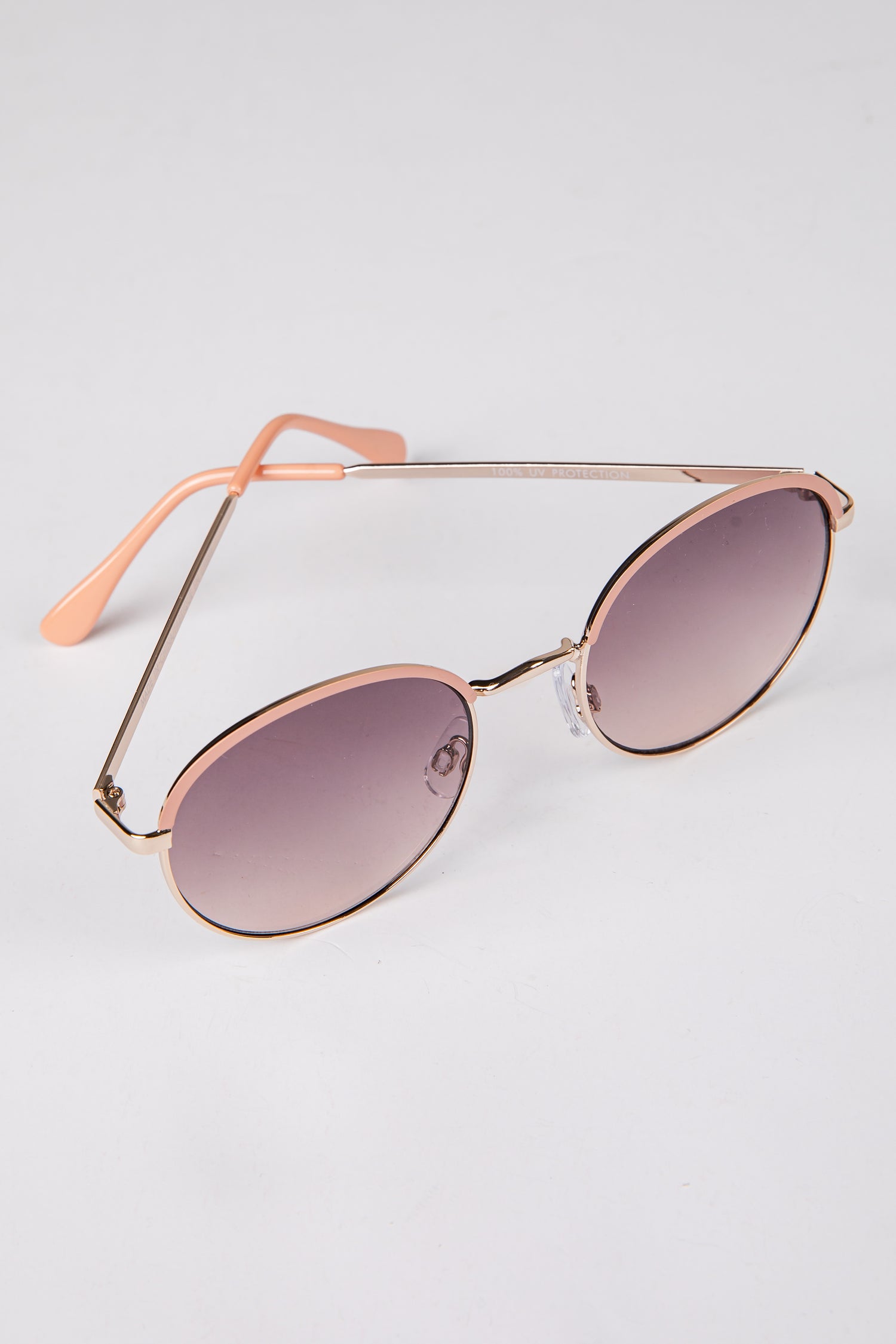 Sunglasses with rose gold frame and gradient lenses on a light gray background
