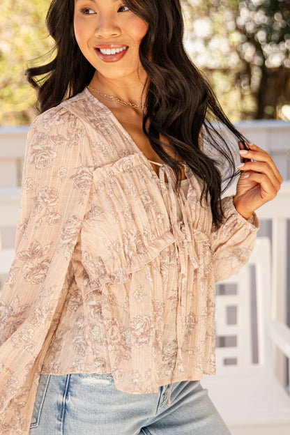 Woman wearing a beige floral blouse and blue jeans outdoors.