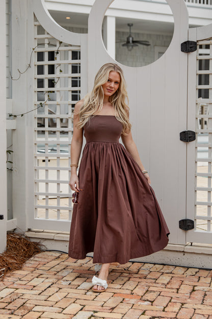 Woman in a brown dress standing in front of a white lattice door.