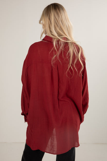 Person wearing a red shirt with long sleeves and a high collar, standing against a plain background.