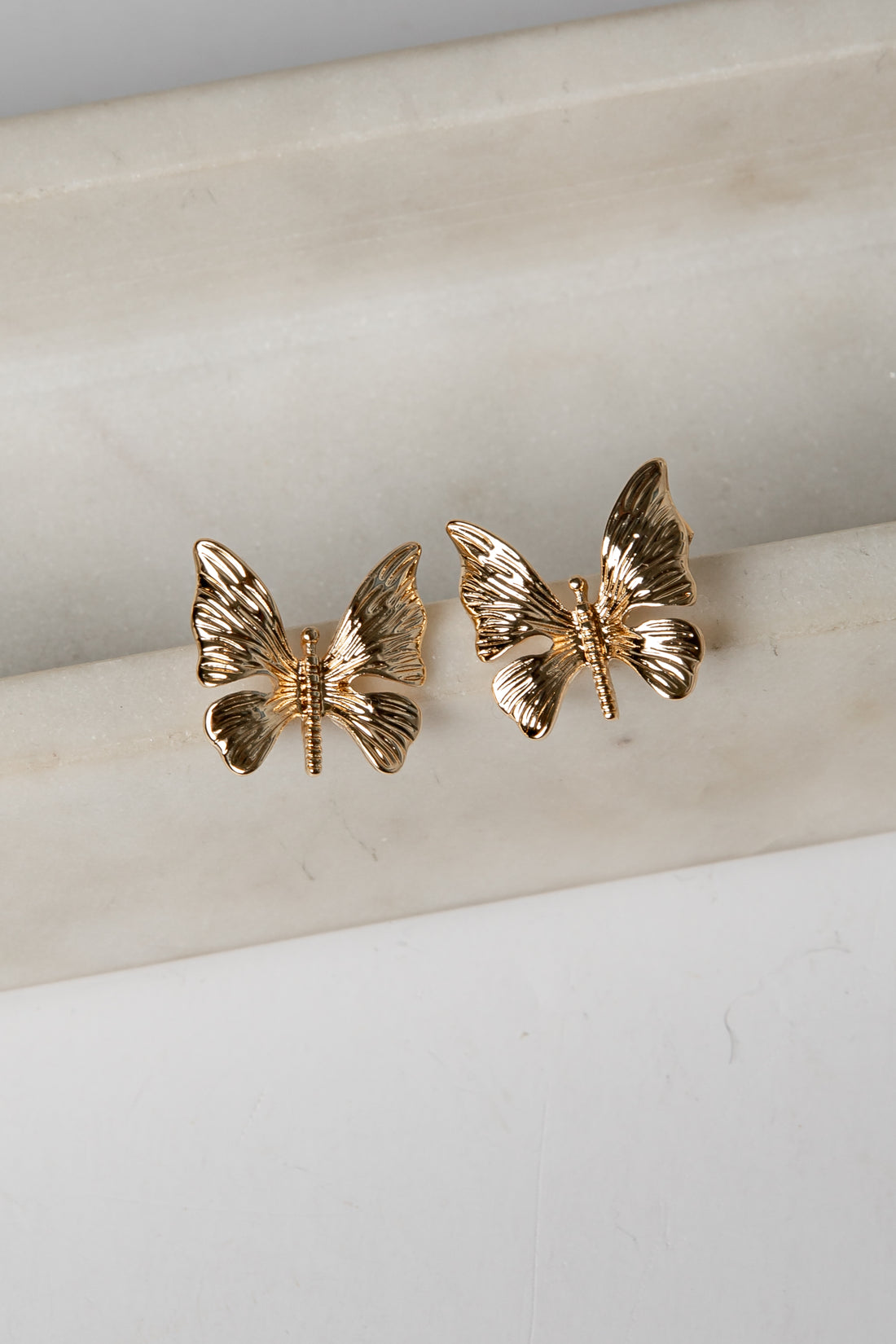 Gold butterfly earrings on a marble surface
