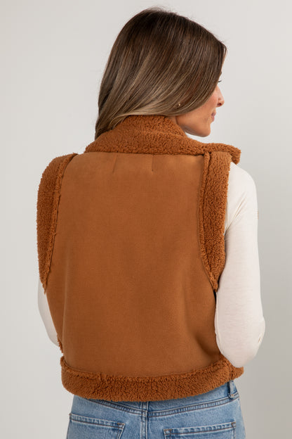 Person wearing a brown fleece vest on a plain background