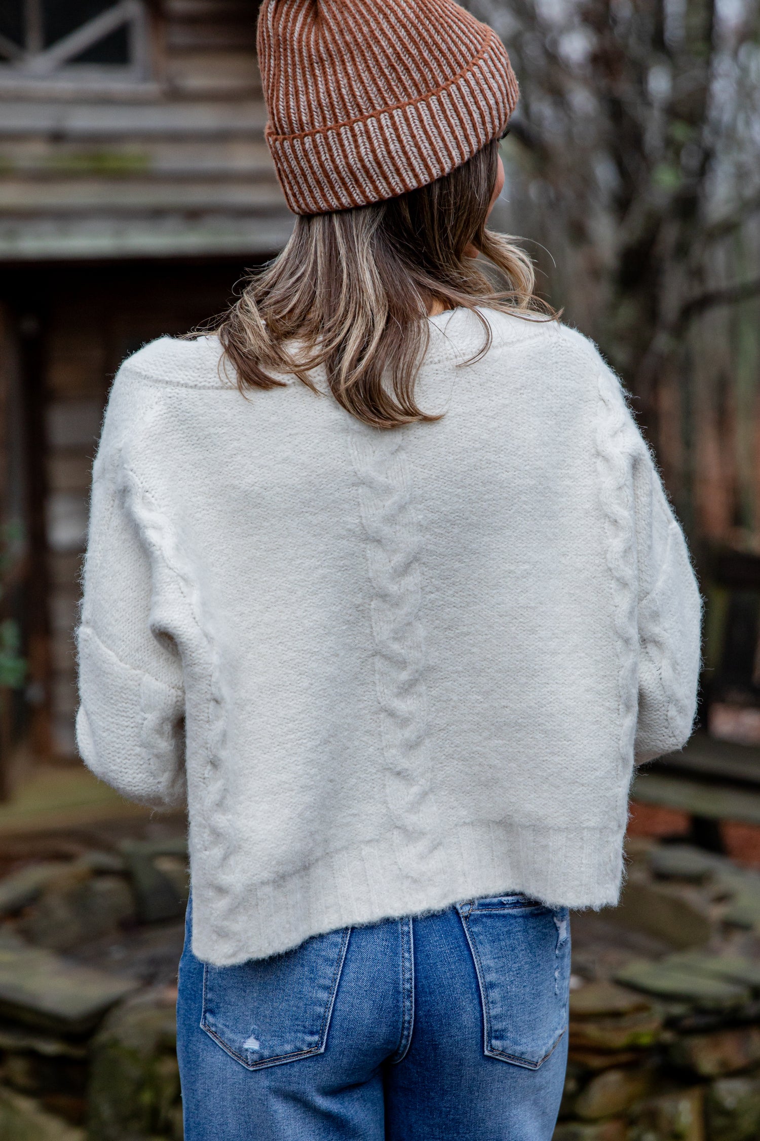 Person wearing a white fluffy jacket and brown beanie with back turned, standing outdoors.