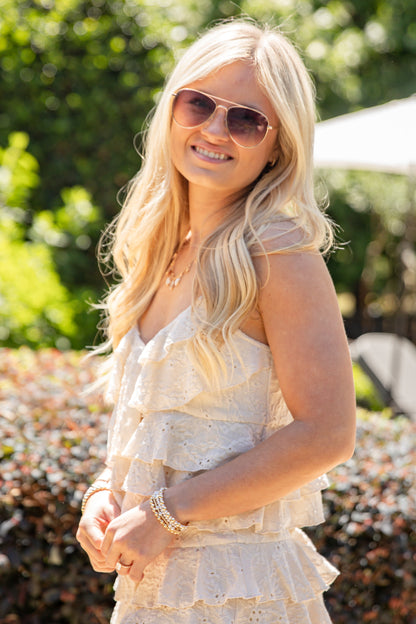 Woman wearing a white dress and sunglasses outdoors with greenery in the background