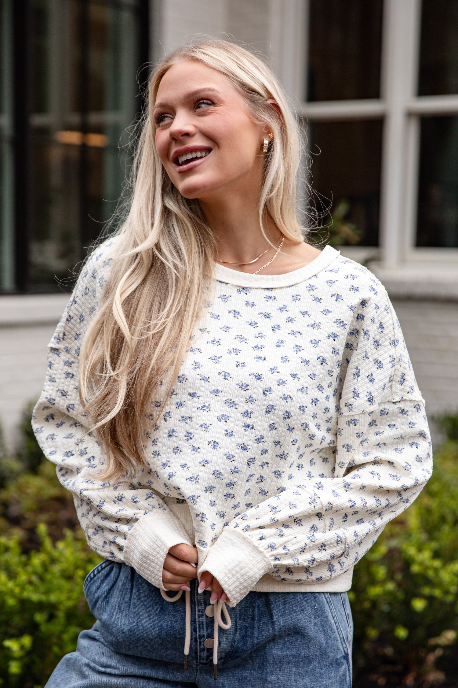 Woman wearing a white floral sweater and blue jeans outdoors.