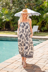 Woman in a leaf-patterned dress standing by a pool with palm trees in the background