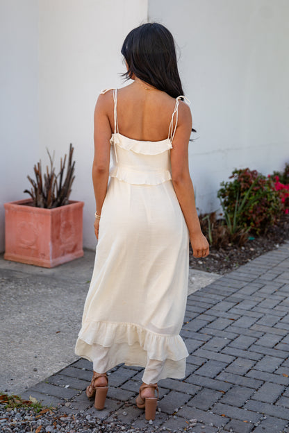 Woman in a white dress walking on a sidewalk with plants and a white wall in the background