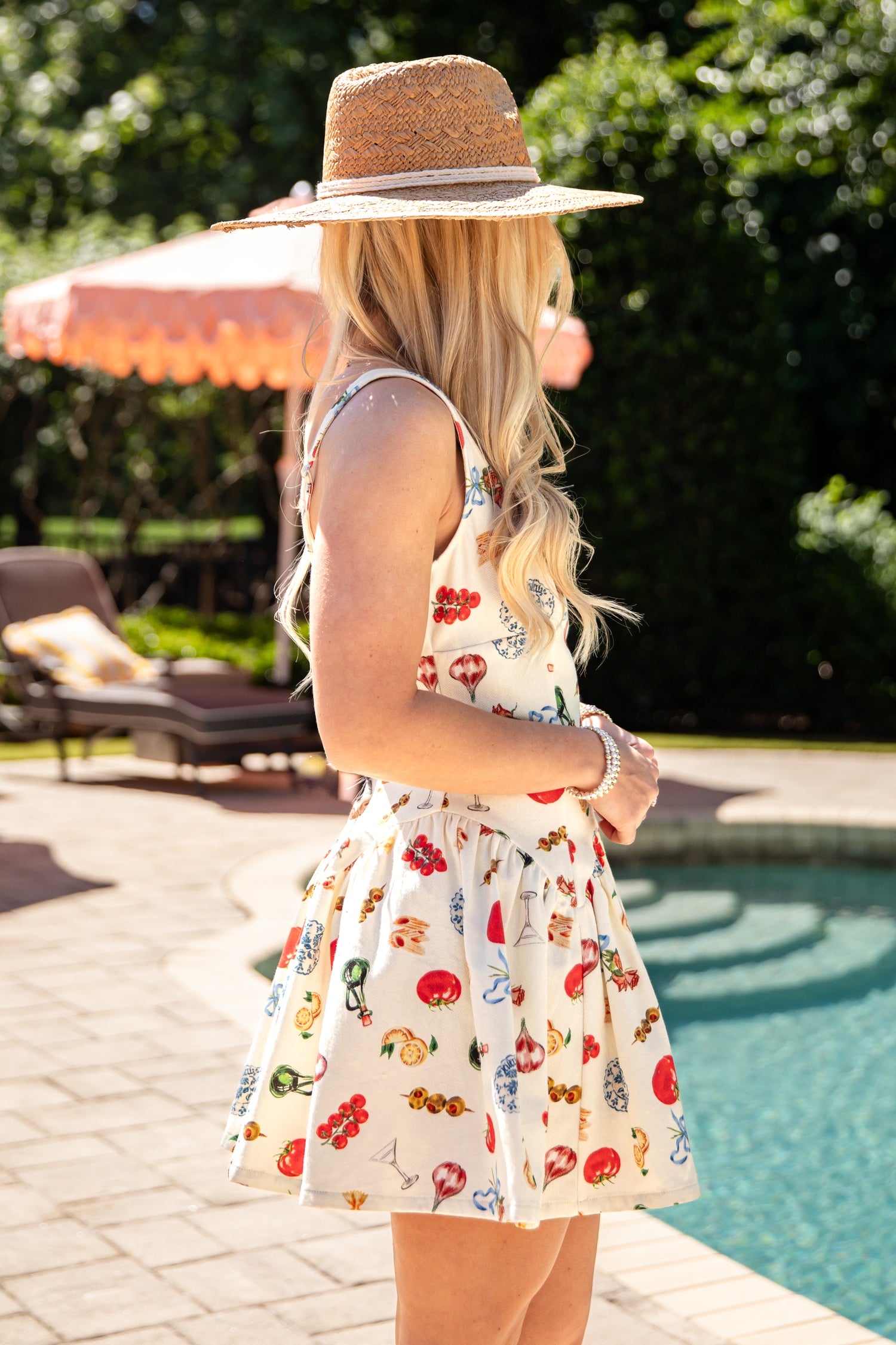 Woman in a floral dress and straw hat by a poolside