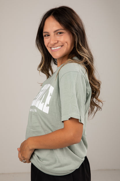 Woman wearing a light green t-shirt with text, standing against a plain background
