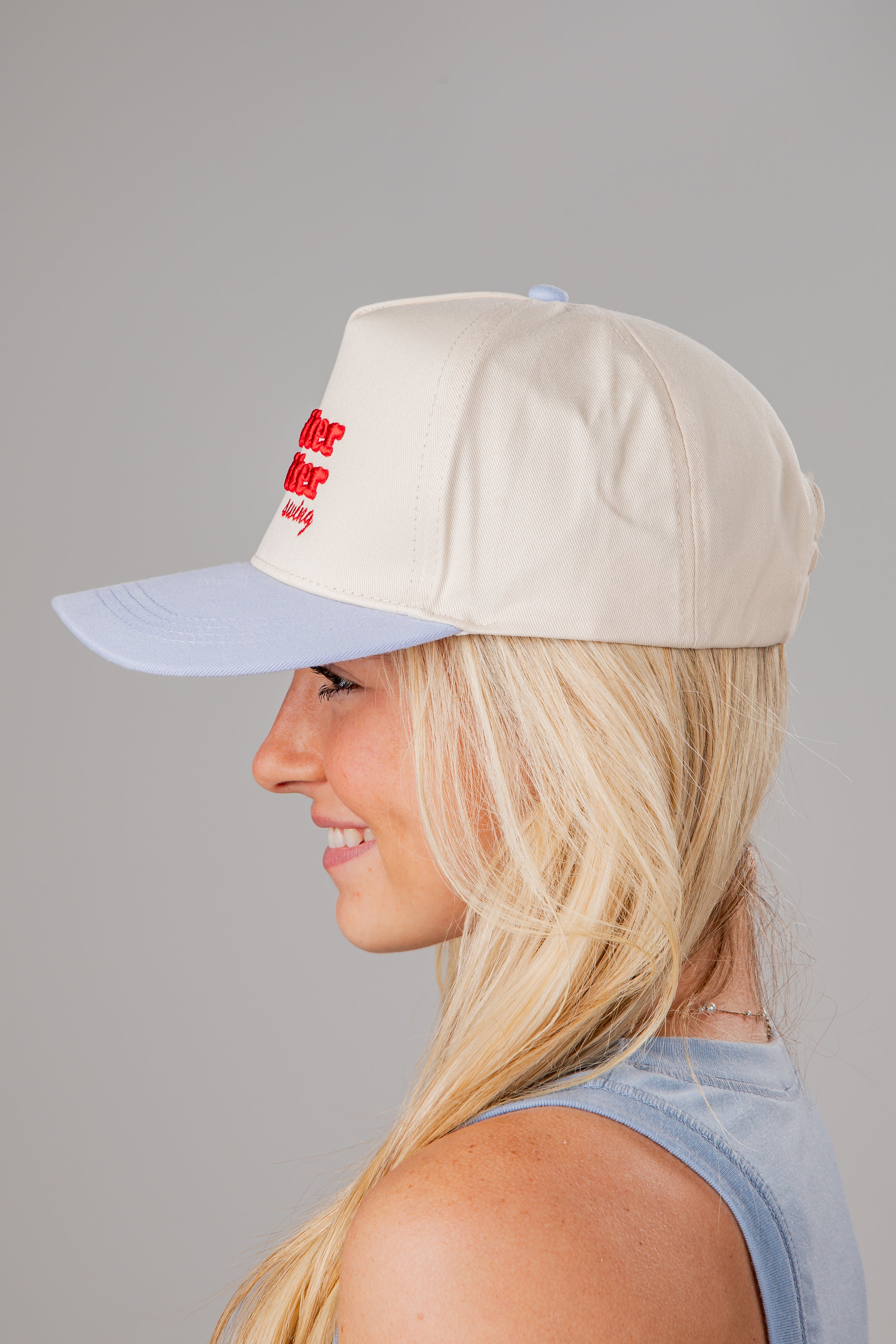 Woman wearing a beige cap with a red logo on a gray background