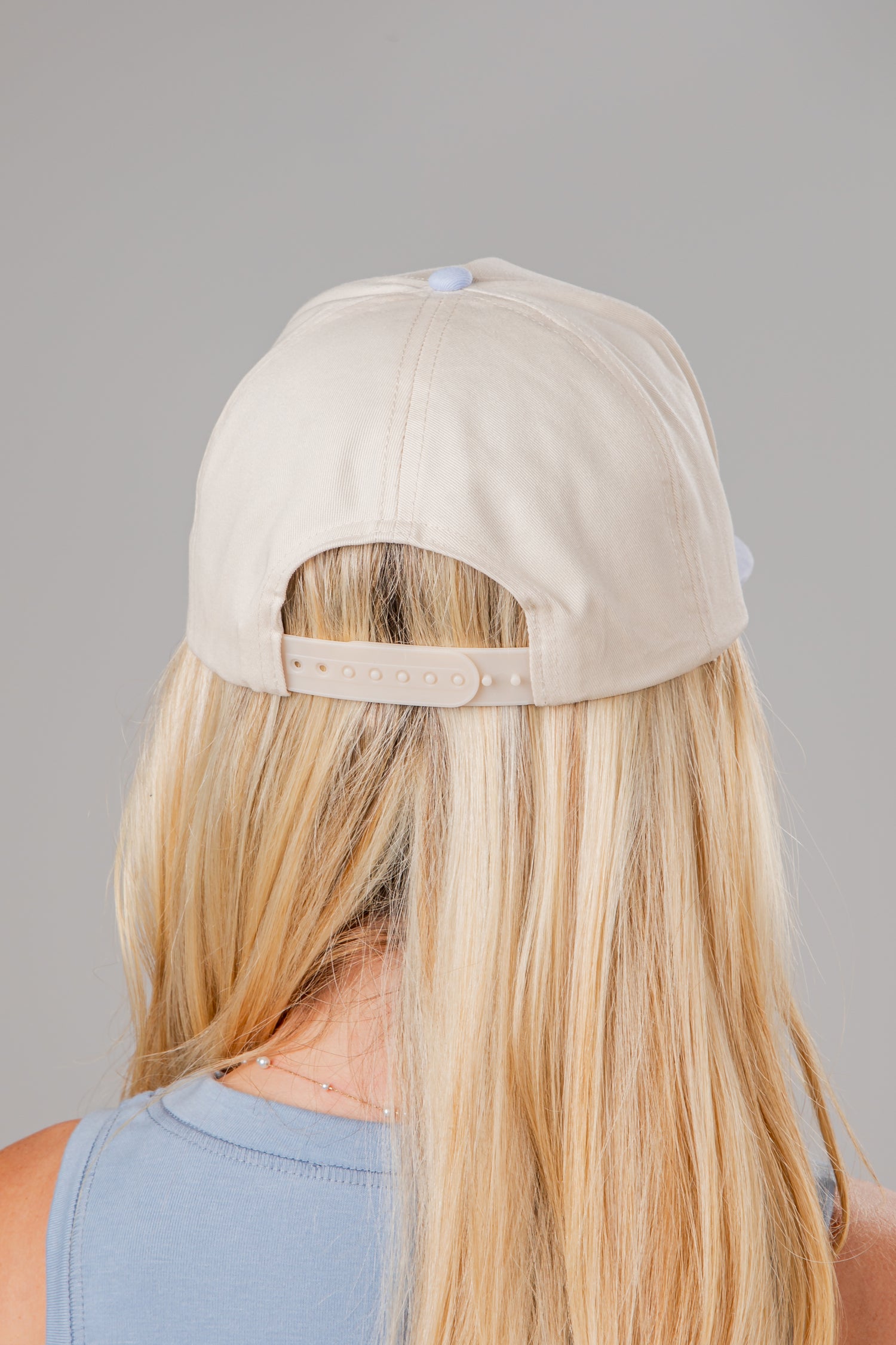 Beige cap worn by a person with blonde hair on a gray background