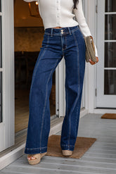 Person wearing blue jeans and a white top, standing on a porch.