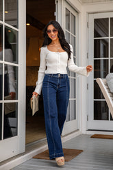 Woman in white top and blue jeans standing on a porch