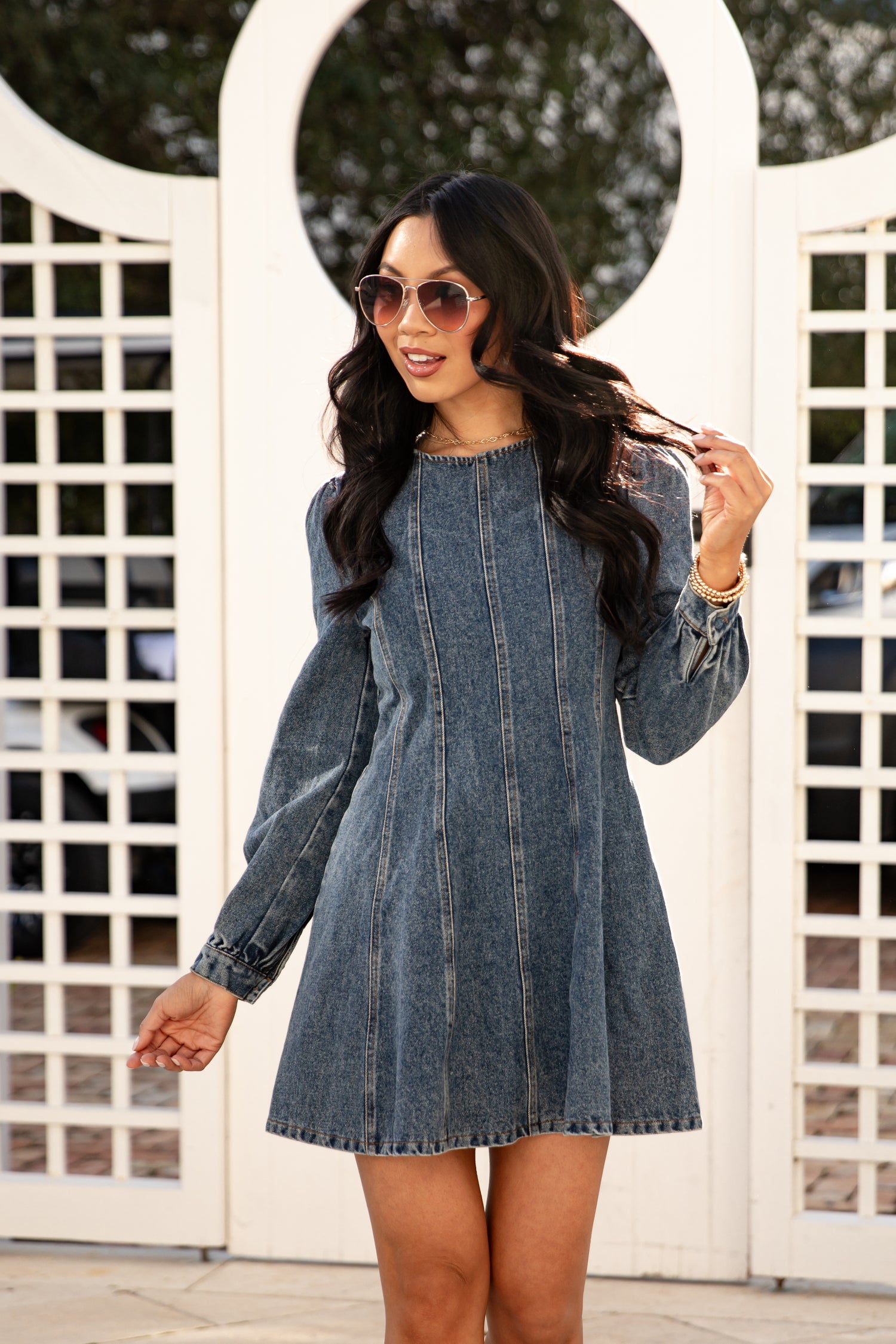 Woman wearing a denim dress in front of a white lattice background