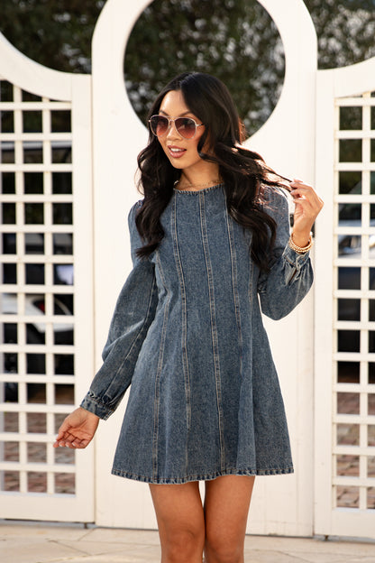 Woman wearing a denim dress in front of a white lattice background