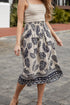 Woman wearing a patterned skirt and beige top on a paved outdoor area.