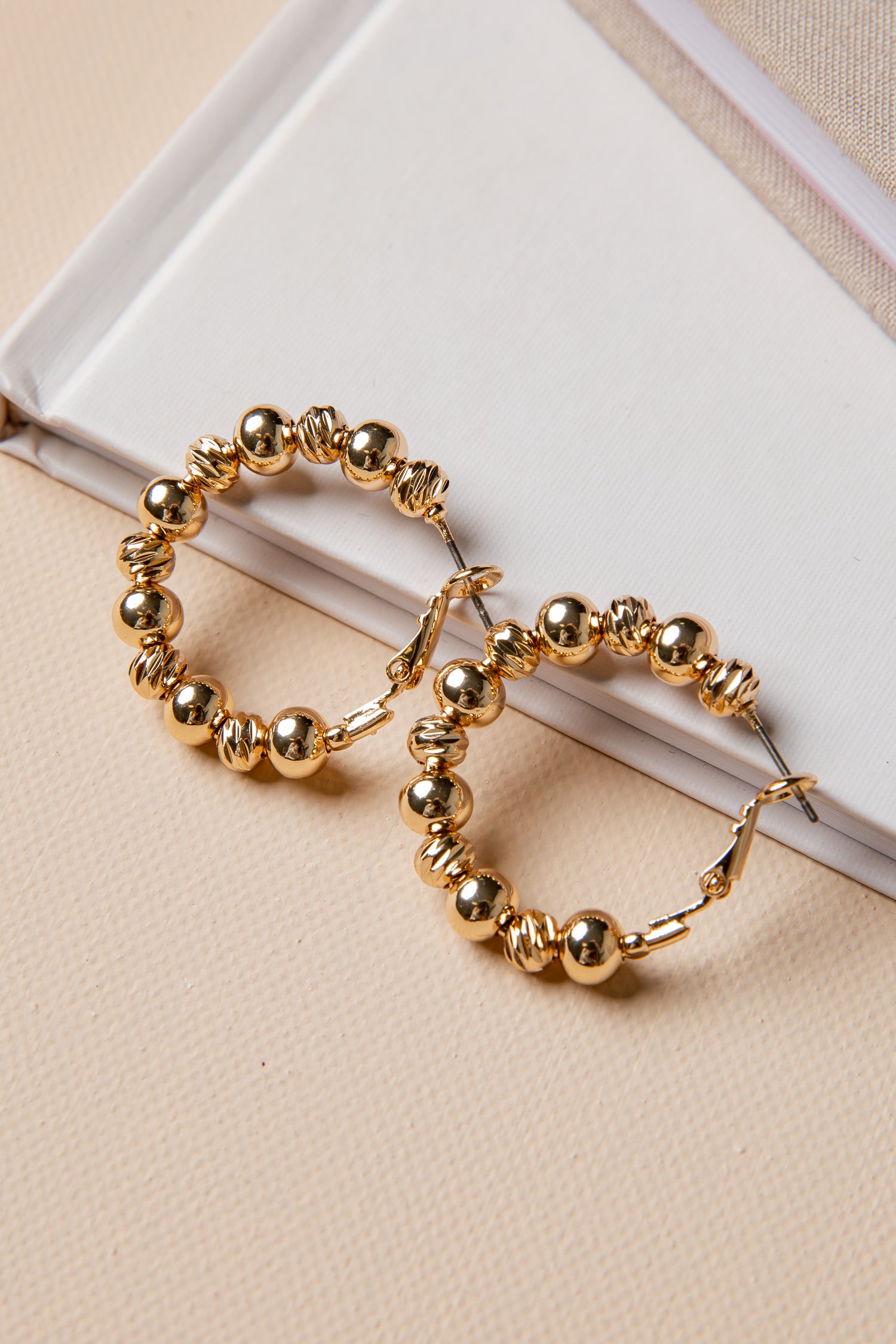 Gold hoop earrings with beaded design on a beige surface
