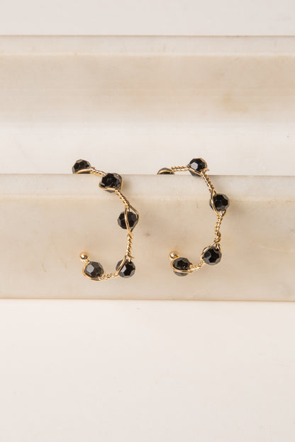 Gold hoop earrings with black gemstones on a beige surface